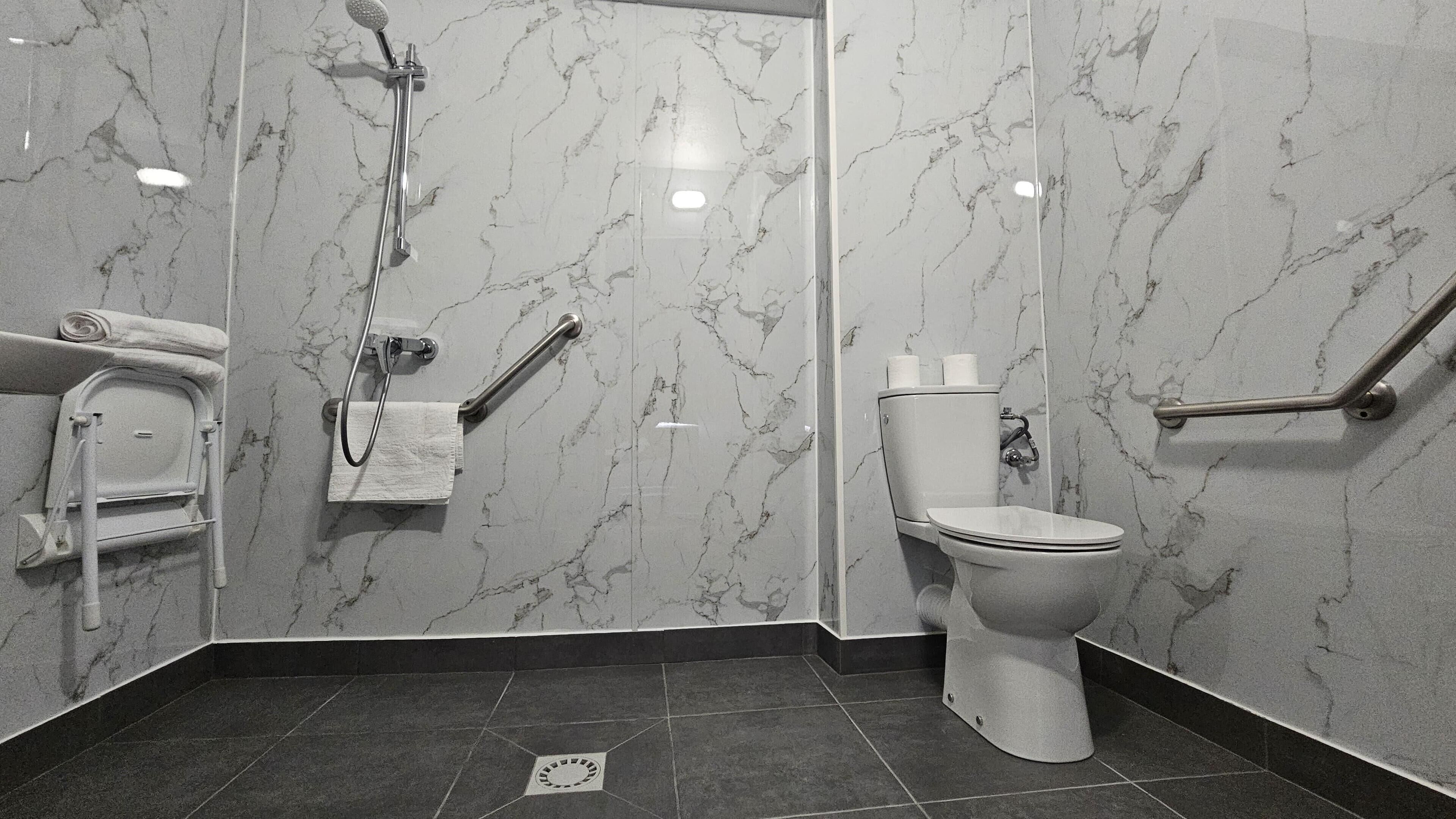 A bathroom with a toilet, a shower, and a handrail.