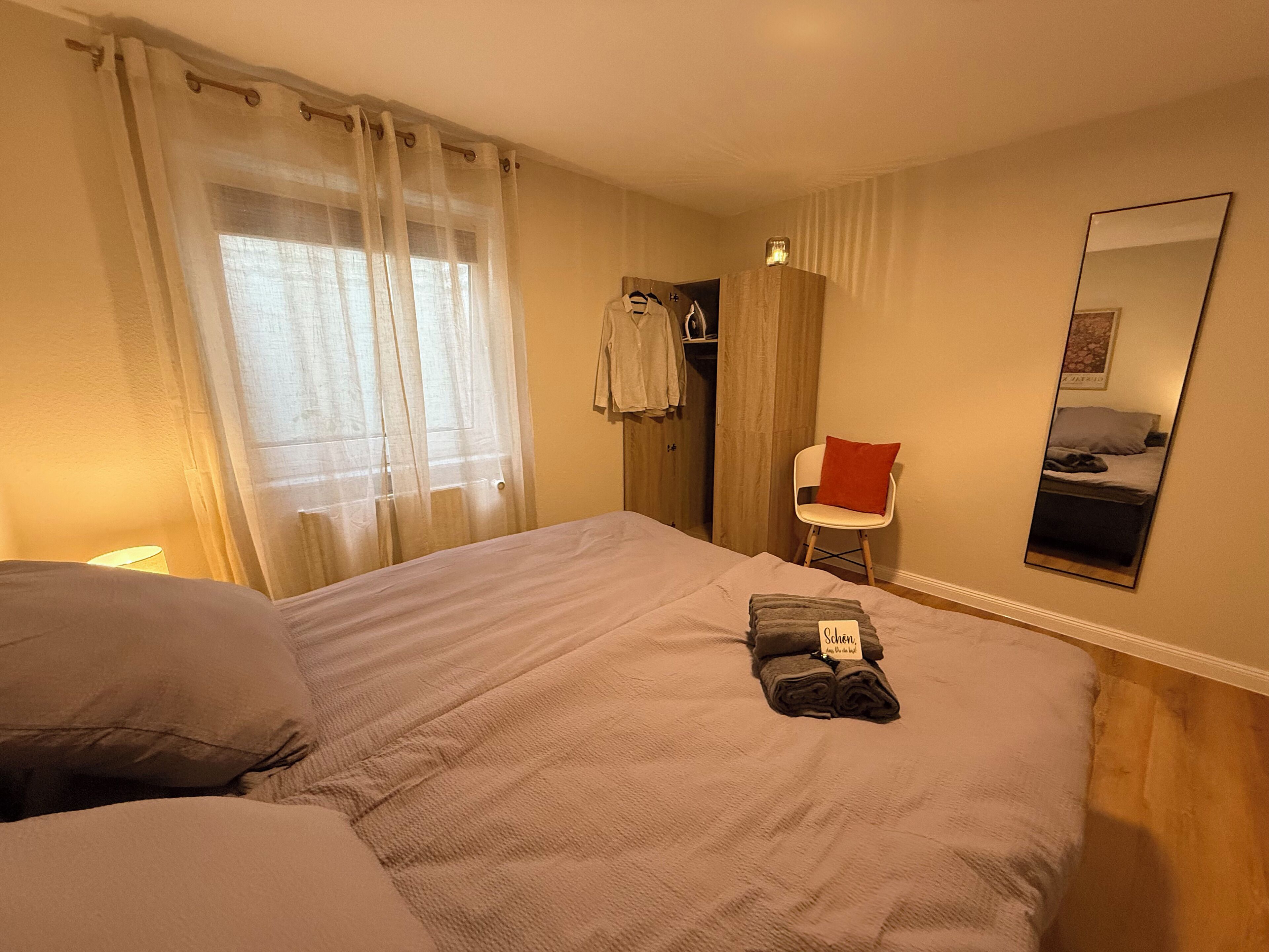 Ein Hotelzimmer mit Bett, Stuhl, Spiegel und einem Fenster mit Vorhängen.