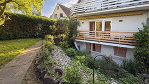 Una casa de dos pisos con un balcón, un jardín con diversas plantas y un camino.