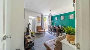 A modern living room with a teal accent wall, a leather sofa, a dining area with a table and chairs, and a kitchen area with a refrigerator and a coffee machine. - Castle View Haven-Quirky and Cosy 5 Bedroom in Strood/Rochester with Castle view (Rochester)