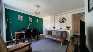 A living room with a green accent wall, a brown sofa, a dining table with chairs, and a TV. - Castle View Haven-Quirky and Cosy 5 Bedroom in Strood/Rochester with Castle view (Rochester)