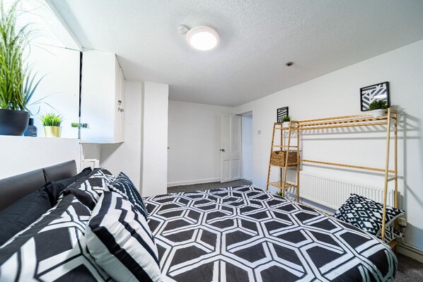 A modern bedroom with a geometric-patterned bedspread, a bunk bed with a ladder, and potted plants on a shelf. - Castle View Haven-Quirky and Cosy 5 Bedroom in Strood/Rochester with Castle view (Rochester)