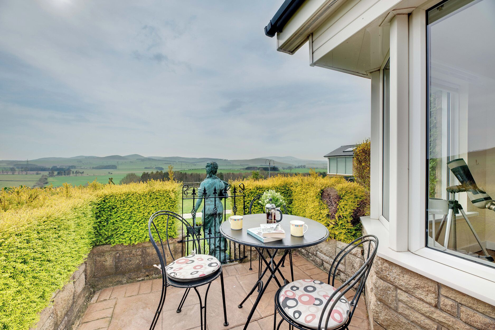 A patio with a table and chairs, a statue, and a view of the countryside.