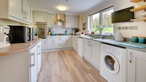 Une cuisine moderne avec des meubles blancs, un four encastré, un four à micro-ondes, une machine à café et un lave-linge.