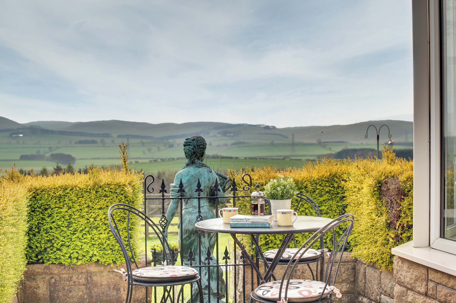 A terrace with a statue, a table, and chairs overlooking a scenic landscape.