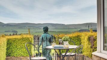 A terrace with a statue, a table, and chairs overlooking a scenic landscape.