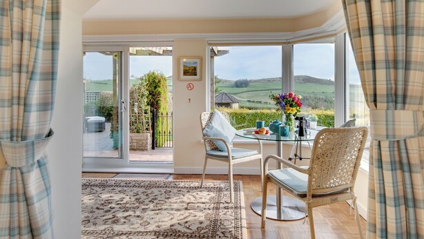 Une pièce dotée d’une porte vitrée donnant sur un patio, d’une table avec des chaises et offrant une vue sur la campagne.