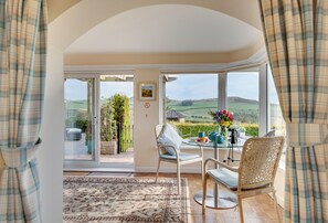 A room with a glass door leading to a patio, a table with chairs, and a view of the countryside. - The Granary (Alnwick)