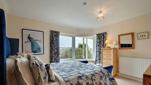 Une chambre à coucher avec un grand lit, une fenêtre avec des rideaux, une commode et un miroir.