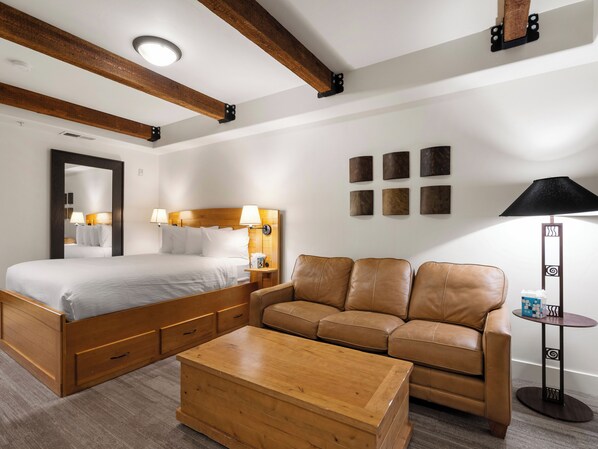 Una habitación de hotel con una cama de madera, un sofá de cuero, una mesita de centro de madera y una lámpara de pie.