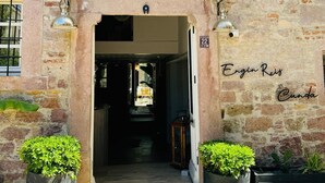 Un bâtiment en pierre avec une porte en bois, deux plantes en pot et une enseigne indiquant « Engin Reis Cunda ».