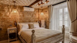 Une chambre avec un mur en pierre, un lit doté d’une tête de lit en bois, deux tables de chevet avec des lampes et une fenêtre avec des rideaux.