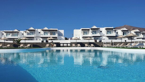 A resort with a swimming pool, white buildings, and a mountain in the background.