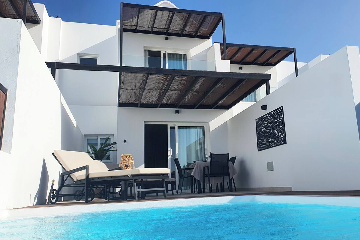 Ein modernes, zweistöckiges Gebäude mit Schwimmbad, Außenbereich zum Sitzen und einer überdachten Terrasse.