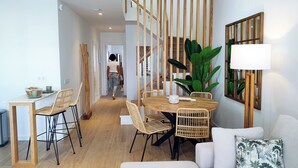 A modern living space with a dining area featuring a wooden table and chairs, a sofa, and a large potted plant.