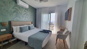 A hotel room with a large bed, a bedside table, a chair, a small table with a bottle, and a view of the outside.