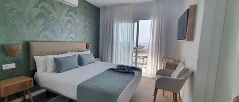 A hotel room with a large bed, a bedside table, a chair, a small table with a bottle, and a view of the outside.