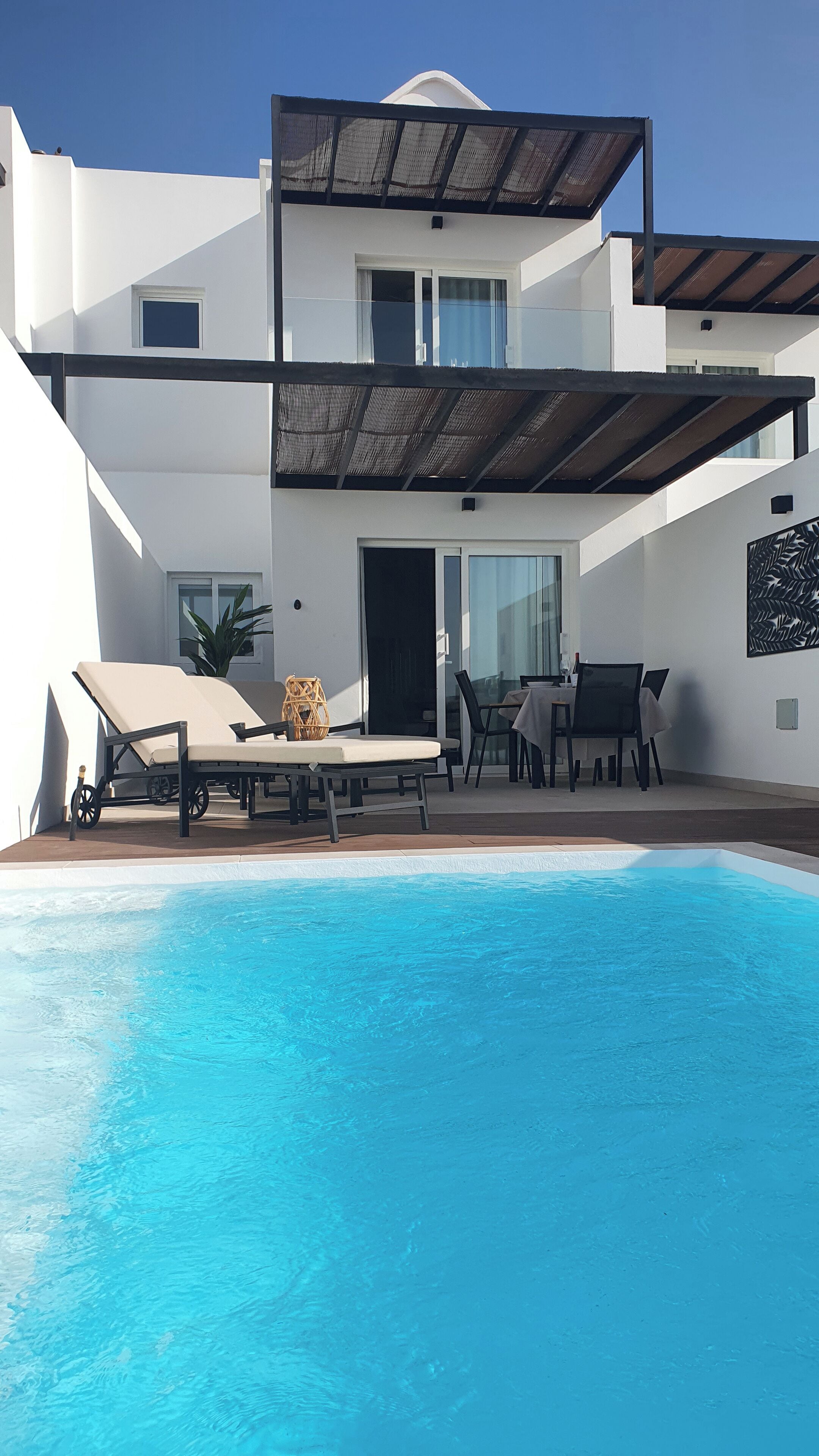 Una casa moderna de dos pisos con piscina, mobiliario exterior y un patio cubierto.