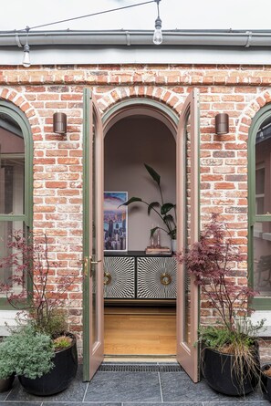 A brick building with a wooden door, two potted plants, and a cityscape poster. - Warm, Comfortable and beautifully decorated! (Dublin)