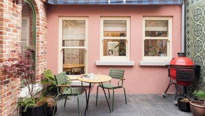 A patio with a brick wall, a wooden table, two chairs, and a red barbecue grill.