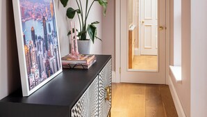 A hallway with a black console, a large framed cityscape picture, a potted plant, and a chandelier.