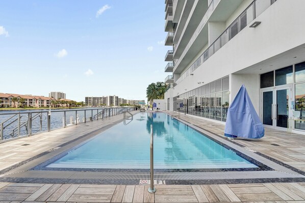 A swimming pool with a view of the water and buildings in the background. - This apartment is a 2 bedroom(s), 2 bathrooms, located in Hallandale, Miami, FL. (Hollywood)