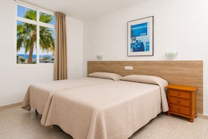 A bedroom with a bed, a nightstand, a window with curtains, a wall-mounted light, and a framed picture.