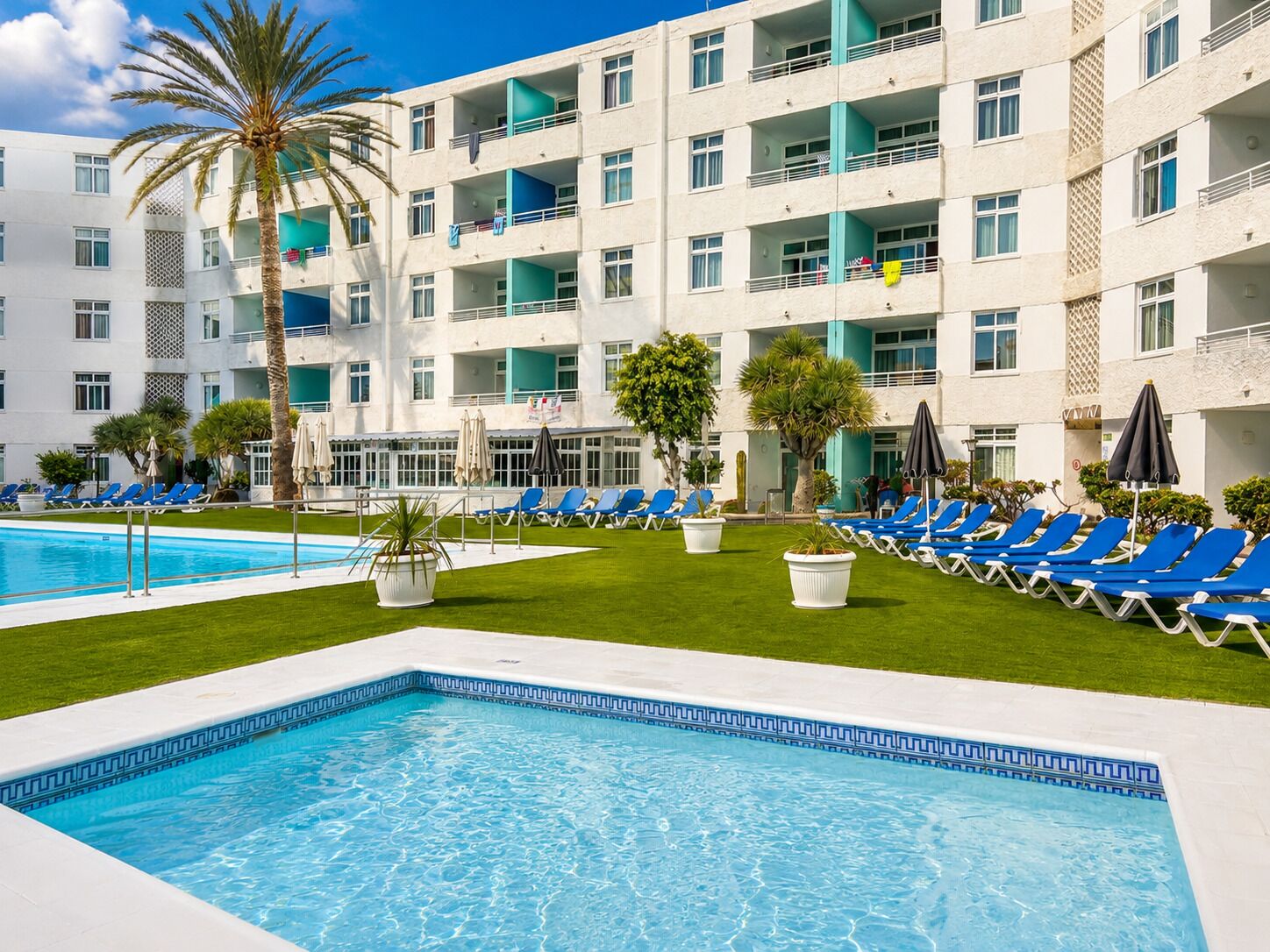 A hotel with a swimming pool, lounge chairs, and a well-maintained lawn.