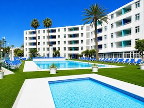 A hotel with a swimming pool, blue lounge chairs, and palm trees. - APARTAMENTOS TAMARAGUA (San Bartolome de Tirajana)