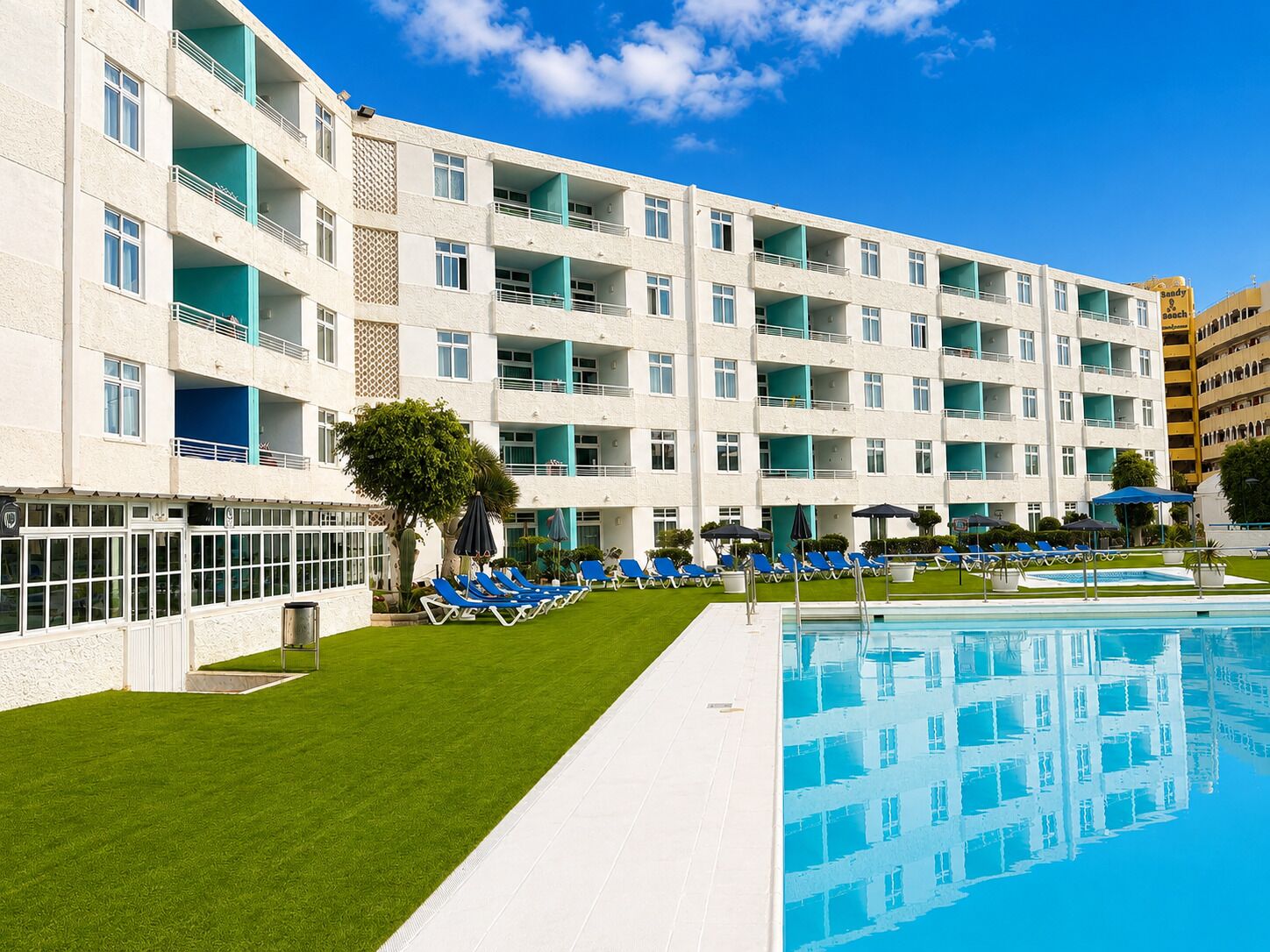 Un hotel de varios pisos con piscina, zona de estar al aire libre y césped bien cuidado.