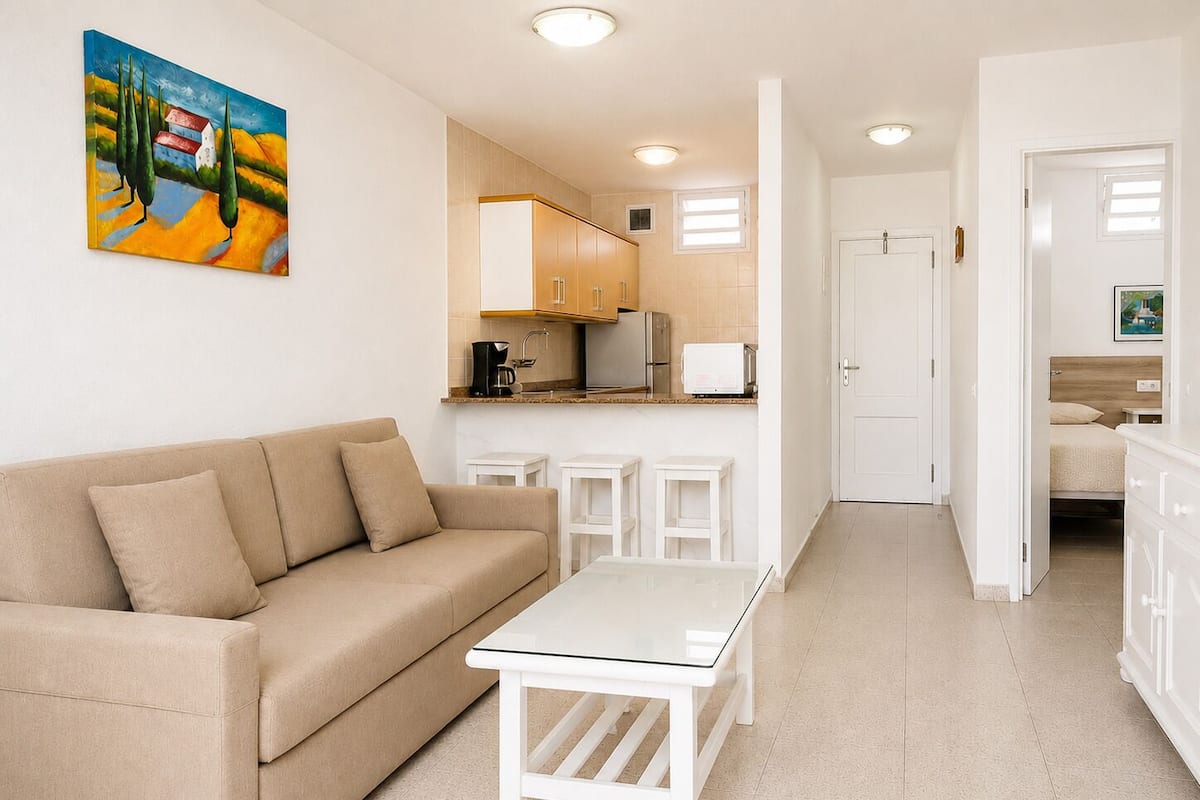 A living room with a beige sofa, a white coffee table, and a painting on the wall.
