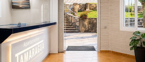 Un espace d’accueil avec une enseigne indiquant « Apartamentos TAMARAGUA », un comptoir de réception, un escalier menant à l’extérieur et une plante en pot.