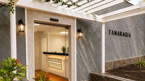 Ein moderner Eingangsbereich mit Glastür, einem Schild mit der Aufschrift 'Apartamentos TAMARAGUA' und einer Steinwand mit Namensschild.