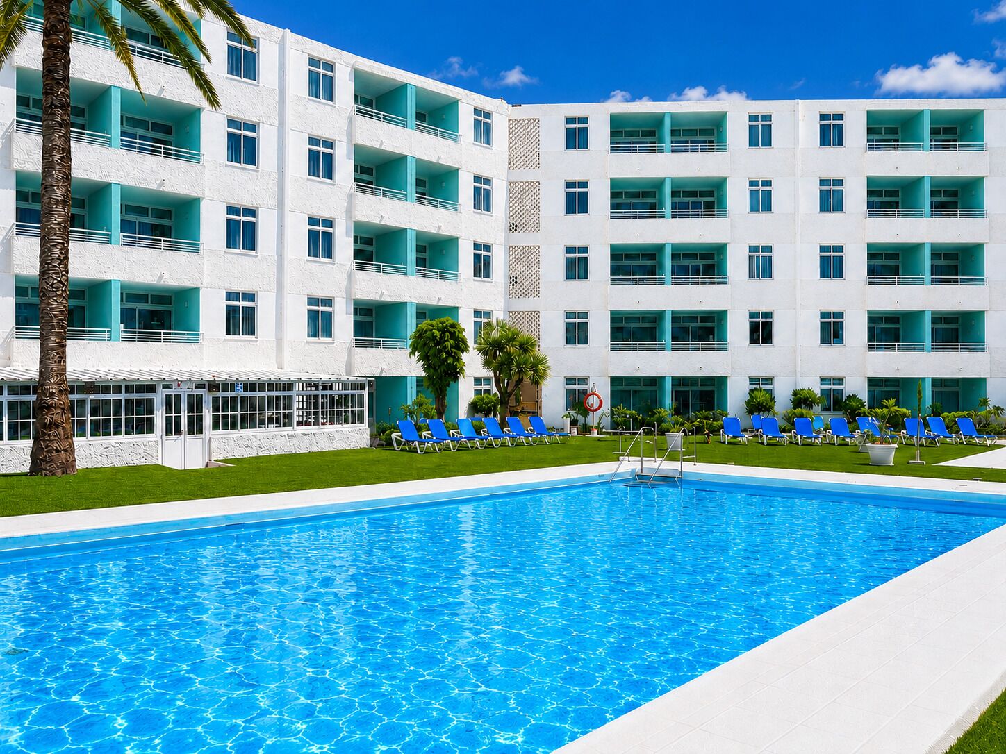 Un hotel con piscina, varios balcones y un césped bien cuidado.