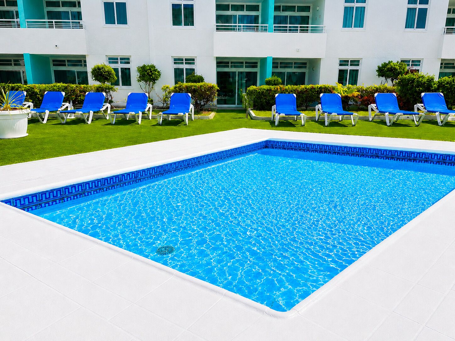 Una piscina rectangular con borde de azulejos azules, rodeada de azulejos blancos y un borde blanco.