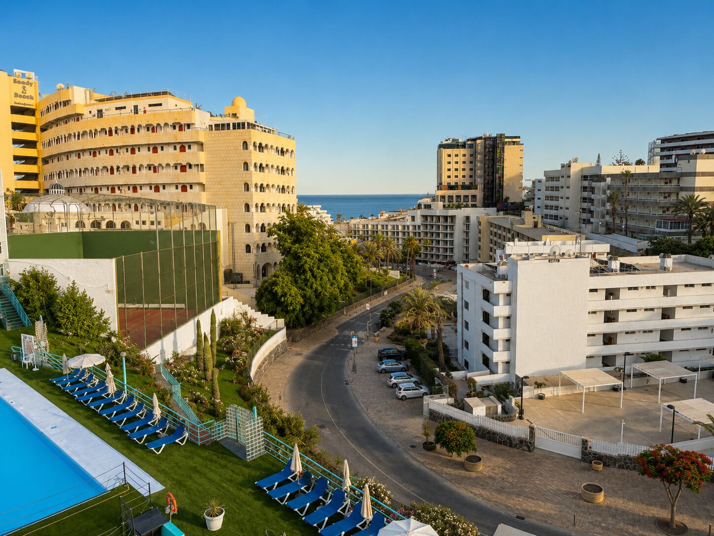 A hotel with multiple floors, a pool area, and a view of the sea.