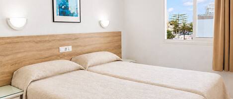 A hotel room with two beds, a wooden headboard, a window with a view of palm trees, and a framed picture on the wall.