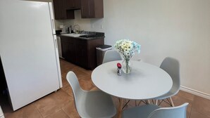 Una cocina compacta con un refrigerador blanco, gabinetes de madera oscura, un lavamanos y una zona de comedor con una mesa redonda y cuatro sillas.