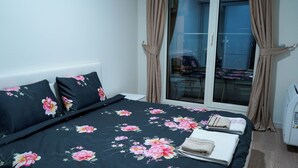Une chambre à coucher avec un lit, une literie à motifs floraux, une fenêtre avec des rideaux et une vue sur l’extérieur.