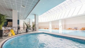 Une piscine intérieure dotée d’un toit en verre, de chaises longues et d’un espace bar.