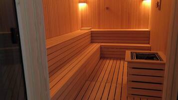 A sauna with wooden benches and walls, a ventilation system, and two wall-mounted lights.