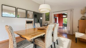 A dining area with a wooden table and woven chairs, a hanging light fixture, and a view into the kitchen and dining room. - Country house with private pool, quiet comfort & nature (Seillans)