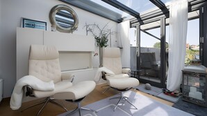 Een moderne kamer met twee witte leren fauteuils, een ronde spiegel, een lijst met een afbeelding en een potplant.