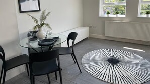 A modern dining area with a glass table, black chairs, a black and white rug, a white bench, and a framed artwork on the wall. - By Allerton Manor & Beatles Spots | Free Parking (Liverpool)