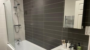 A modern bathroom with a bathtub, a glass-enclosed shower, and a sink with toiletries. - By Allerton Manor & Beatles Spots | Free Parking (Liverpool)