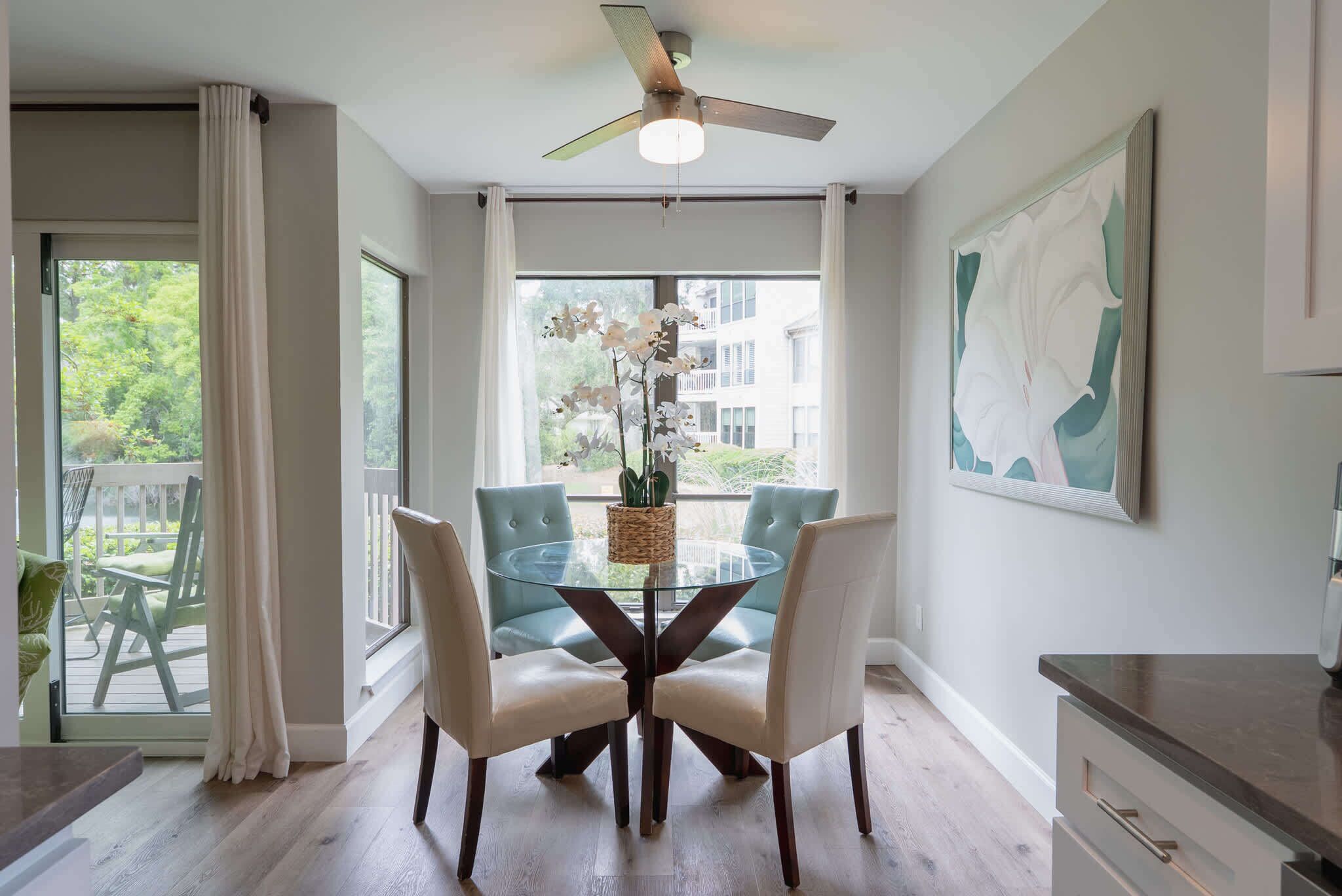 A dining area with a glass table, two chairs, a ceiling fan, and a view of the outdoors.
