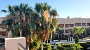 Un balcon donnant sur un quartier résidentiel, avec une rue bordée de voitures garées et un immeuble doté de plusieurs balcons.