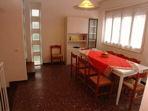 Un coin repas avec une table dressée pour six personnes, une chaise, un petit meuble et une fenêtre avec des rideaux.