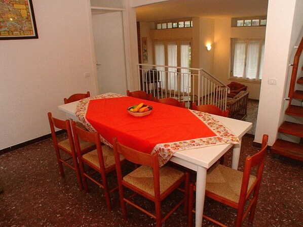 A dining area with a red tablecloth, wooden chairs, and a fruit bowl. - Nice an Welcoming Villa With Patio and Garden (Lignano Sabbiadoro)