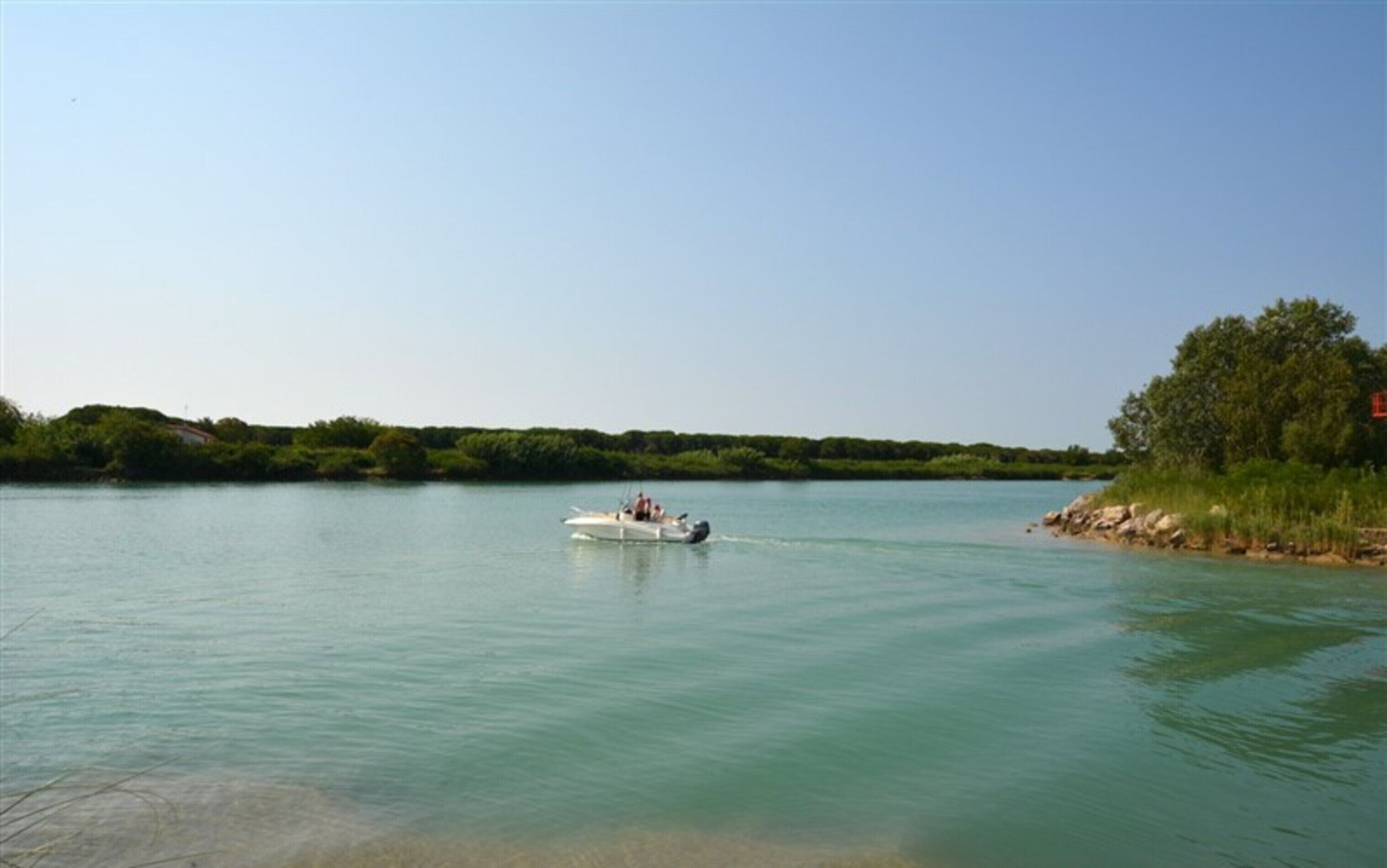 A boat on a calm river with a forested bank and a clear sky.